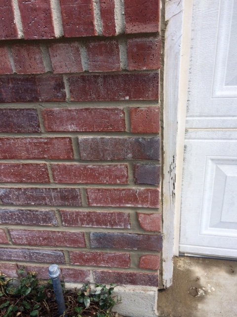 Brick wall adjacent to a garage door showing masonry cracks and mortar deterioration